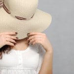 Woman covering her face with a hat being quite shy.